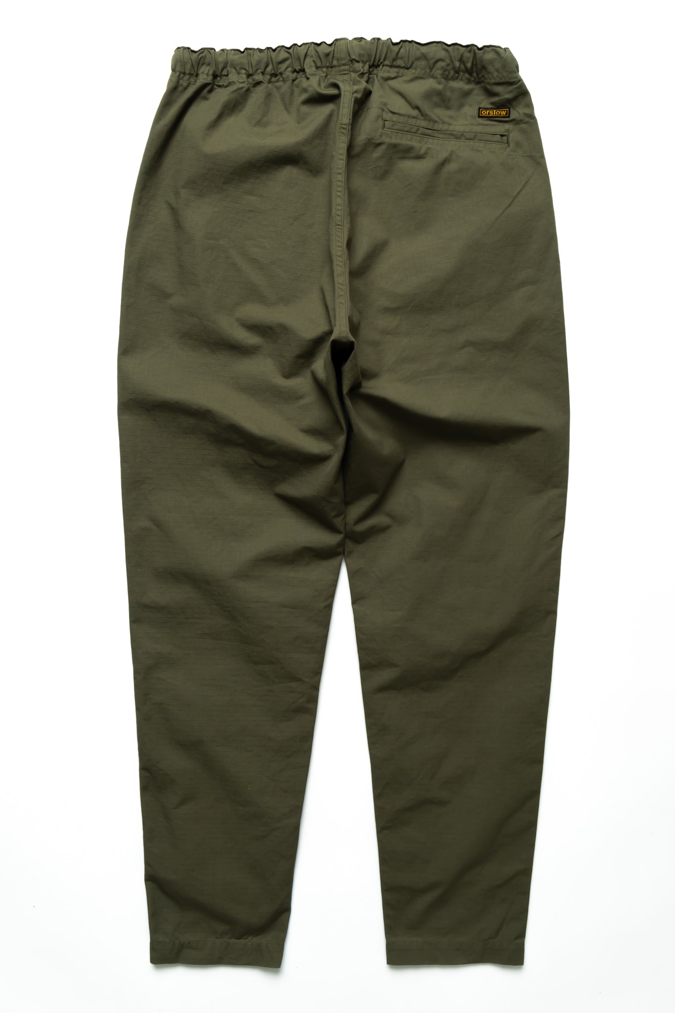 Easy to wear Orslow trousers with an elastic waist and cord drawstring made in Japanese 100% cotton ripstop fabric. Straight leg with a slight taper that features two front pockets and one back. Color: Army Green. Fabric: 100% Cotton. Unisex. Made in Japan.